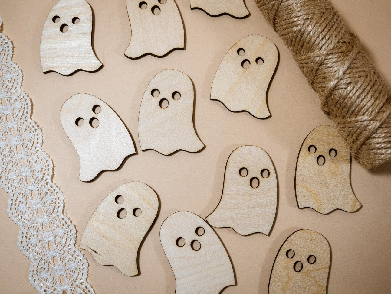 Wooden ghost shapes on a beige surface with twine and lace trim.