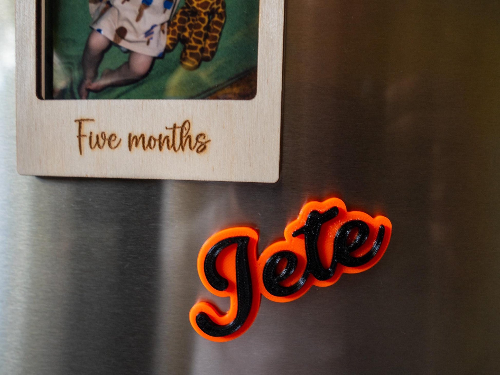 Fridge magnet  on a metallic surface, next to a wooden photo frame with 'Five months' text.