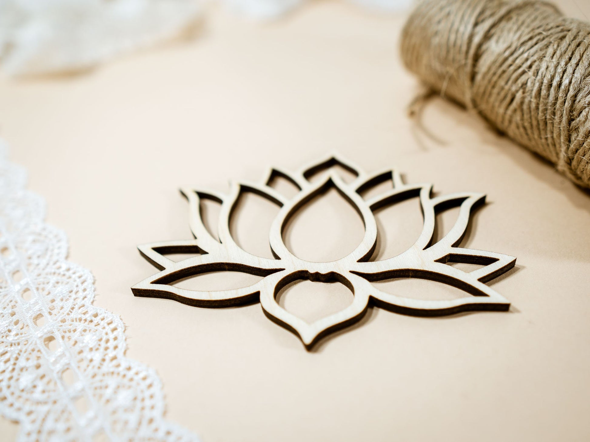 Wooden lotus flower decoration on a beige background with lace and straw elements.