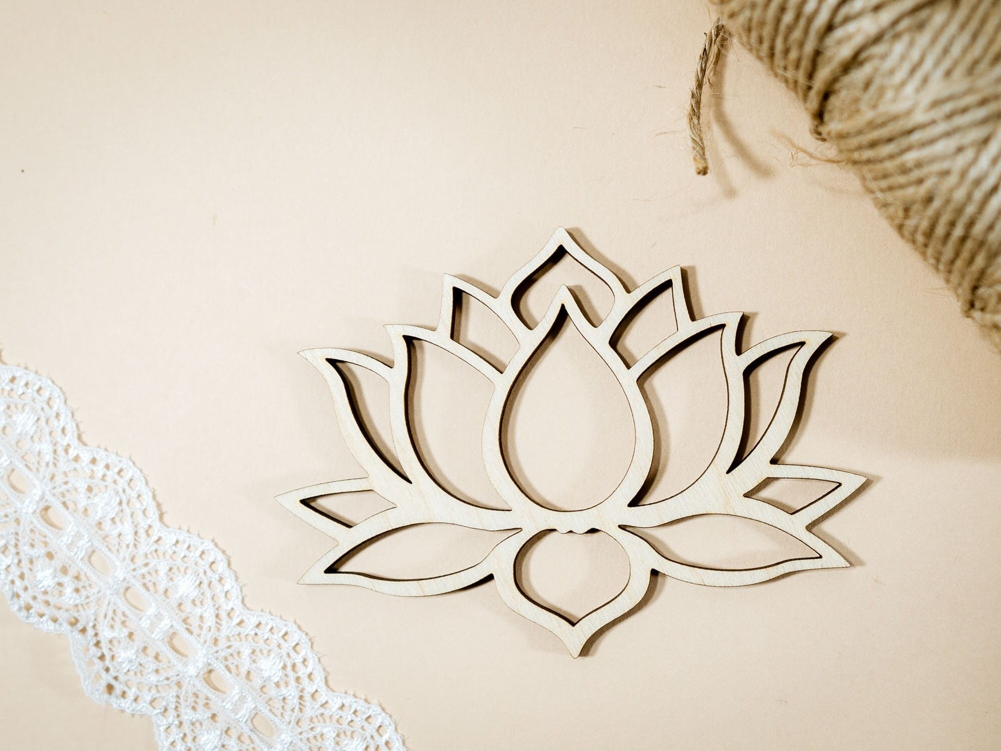 Wooden lotus flower decoration on a beige background with lace and straw elements.