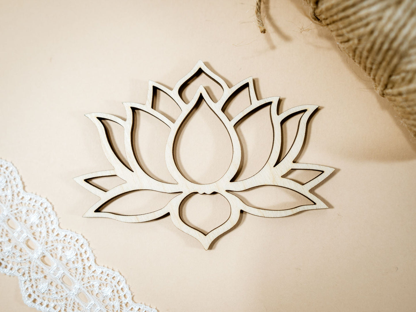 Wooden lotus flower decoration on a beige background with lace and straw elements.
