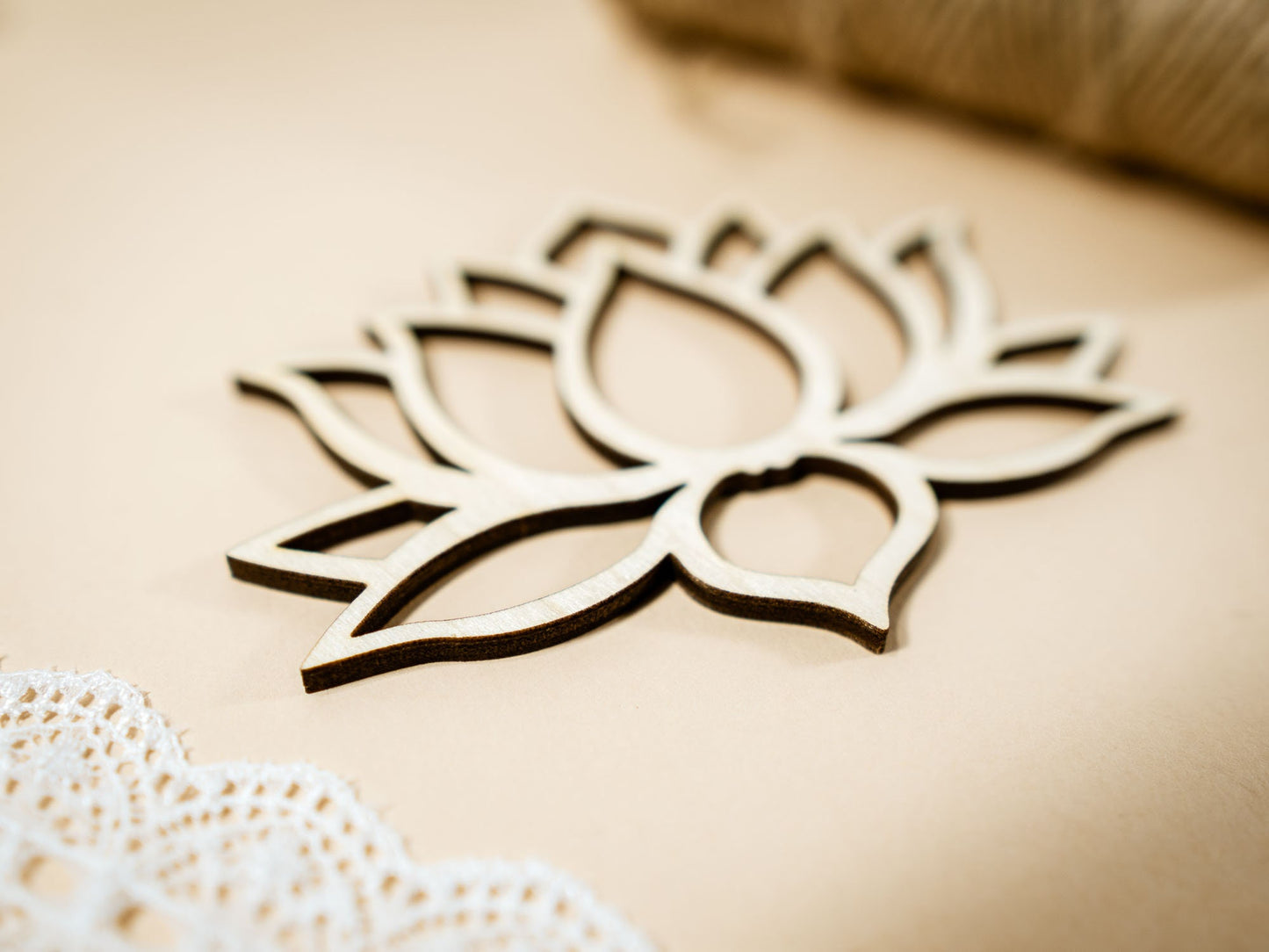 Wooden lotus flower decoration on a beige background with lace and straw elements.