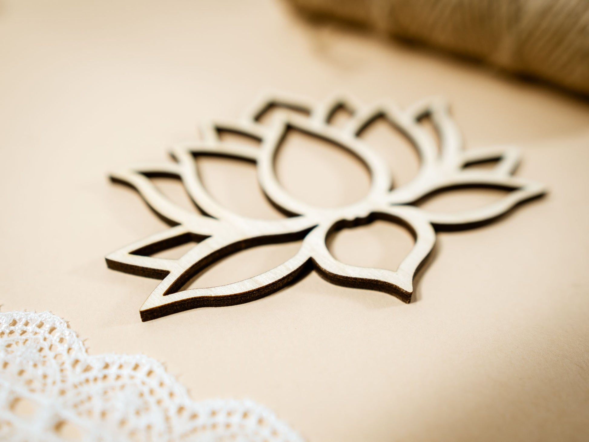 Wooden lotus flower decoration on a beige background with lace and straw elements.