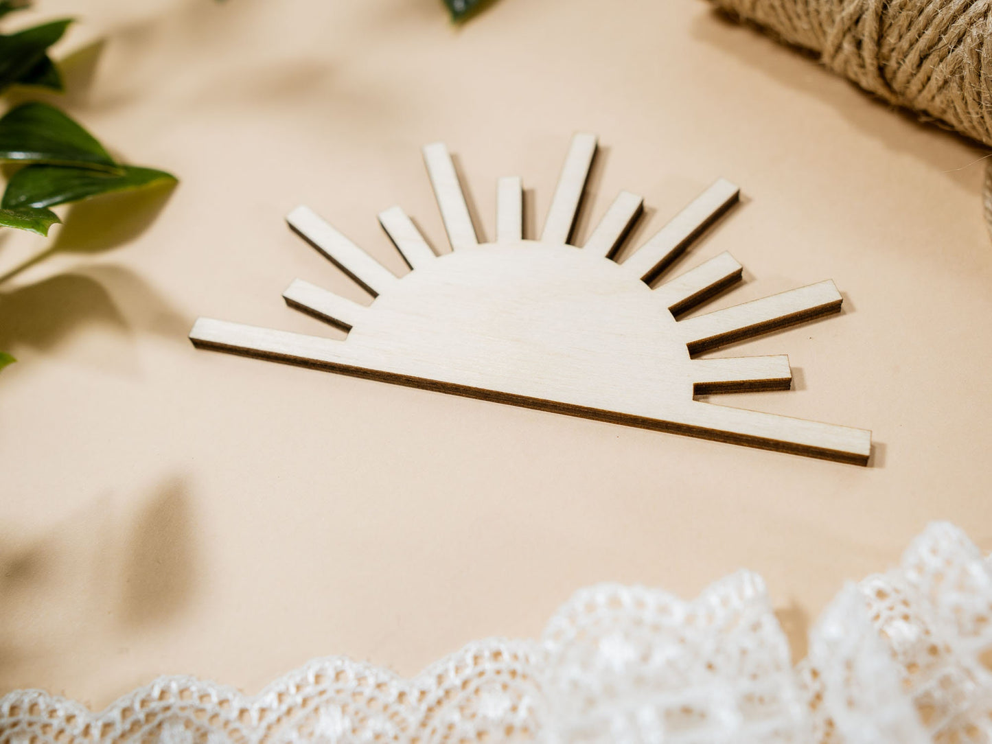 Wooden sun-shaped decor item on a beige surface with lace and leaves.