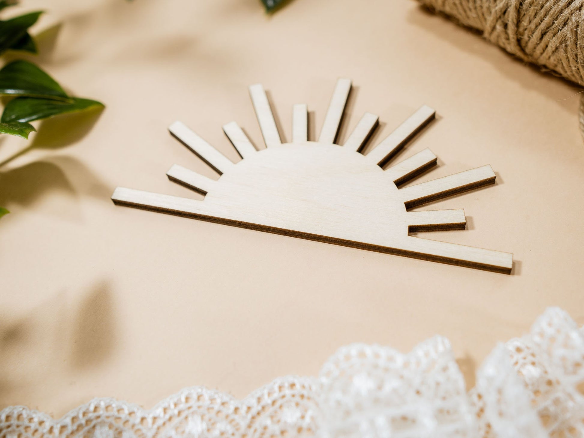 Wooden sun-shaped decor item on a beige surface with lace and leaves.