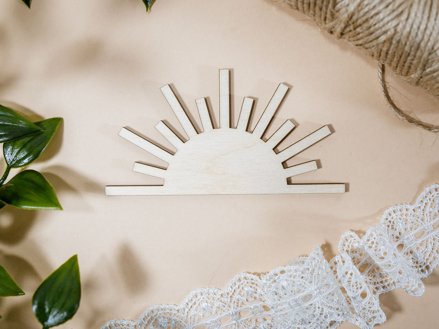 Wooden sun-shaped decor item on a beige surface with lace and leaves.