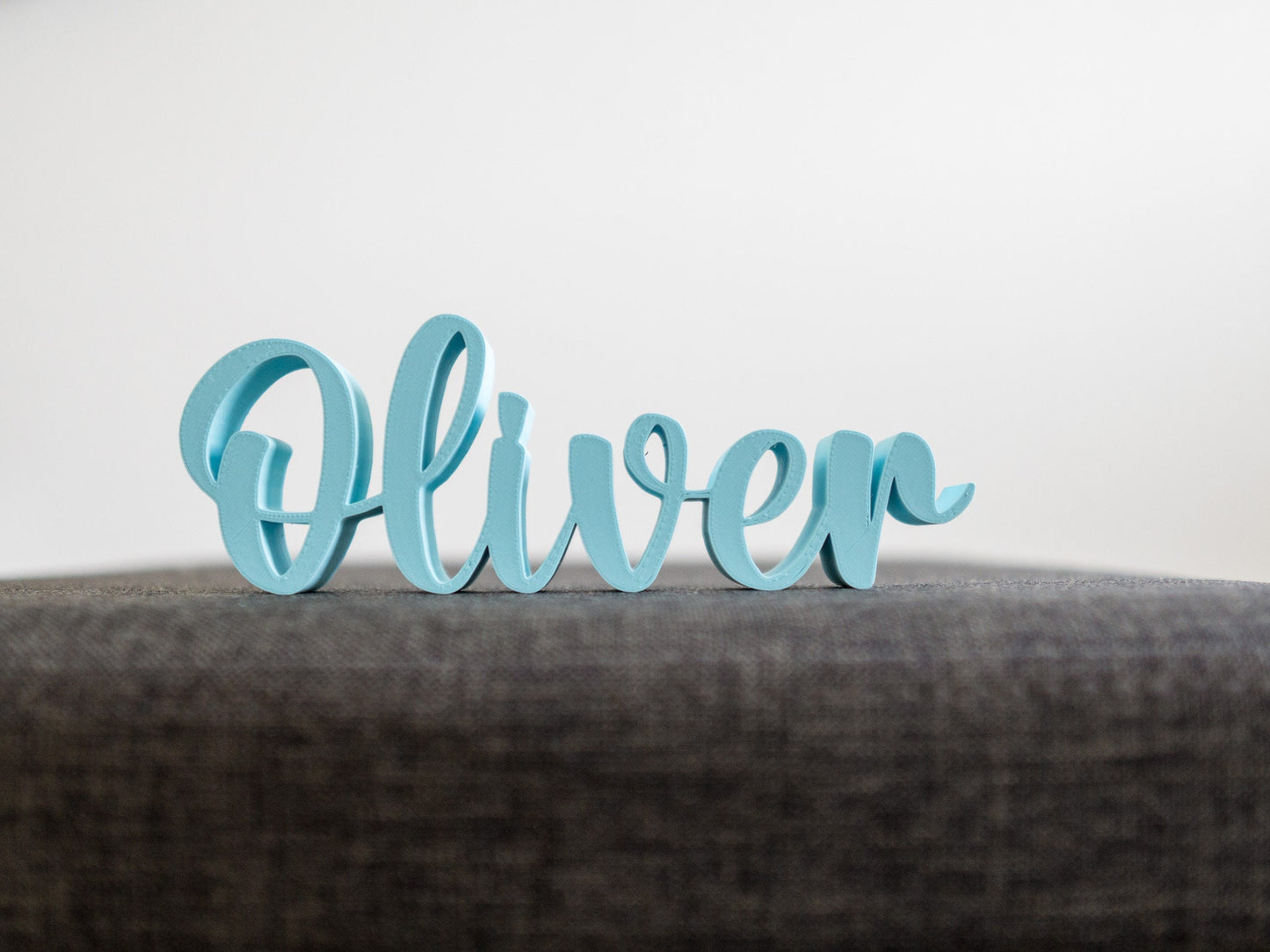 Blue decorative name 'Oliver' on a gray surface with a light gray background