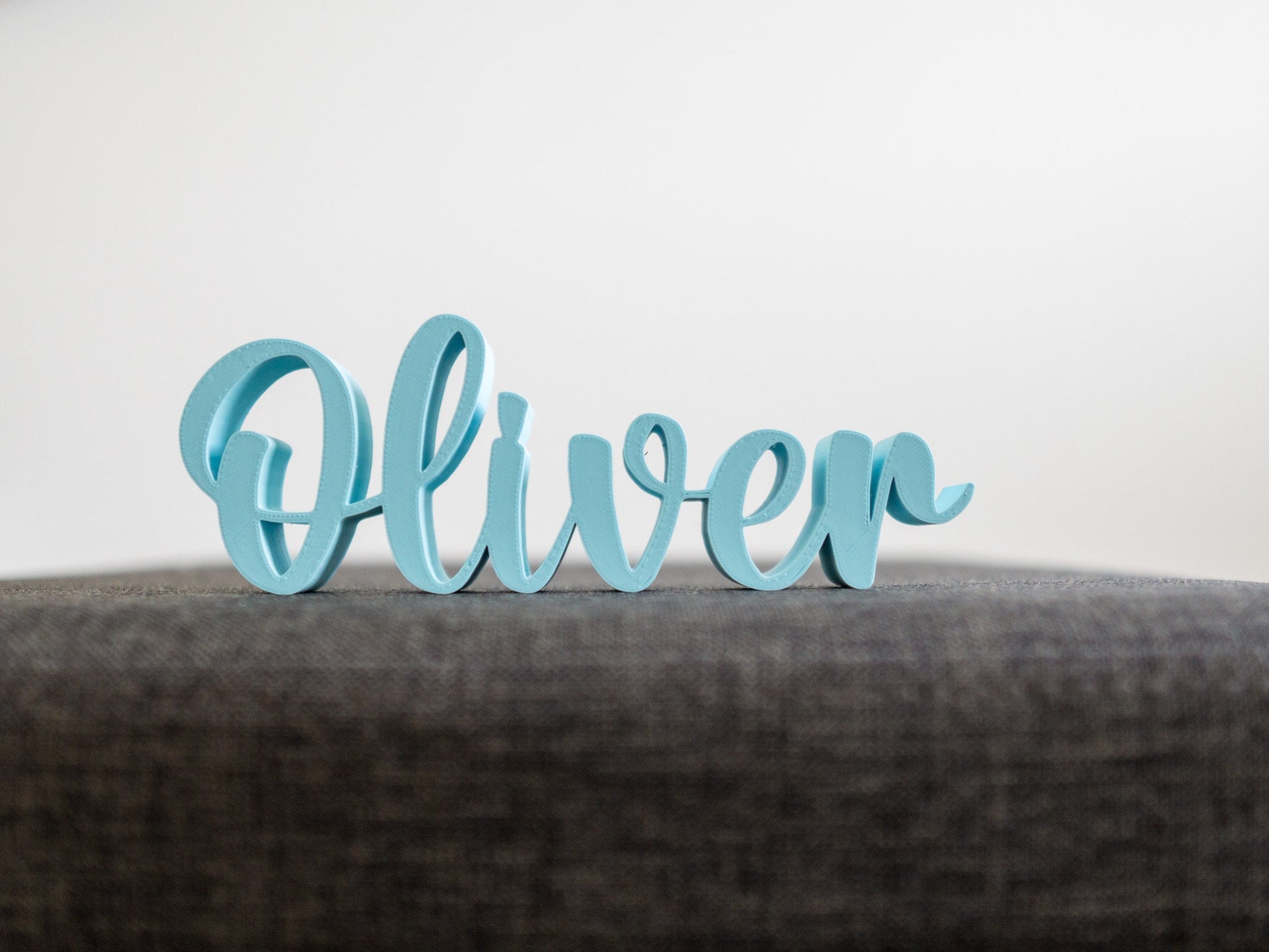 Blue decorative name 'Oliver' on a gray surface with a light gray background