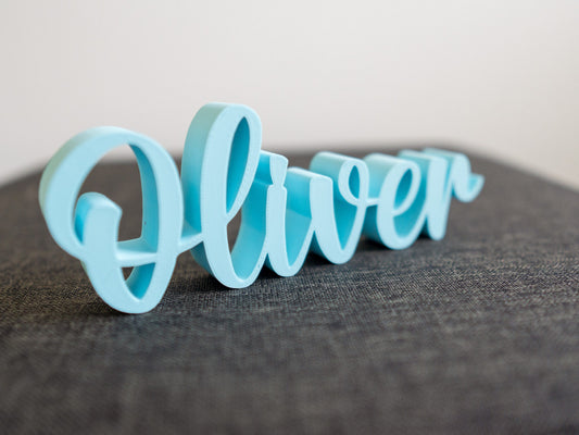 Blue decorative name 'Oliver' on a gray surface with a light gray background