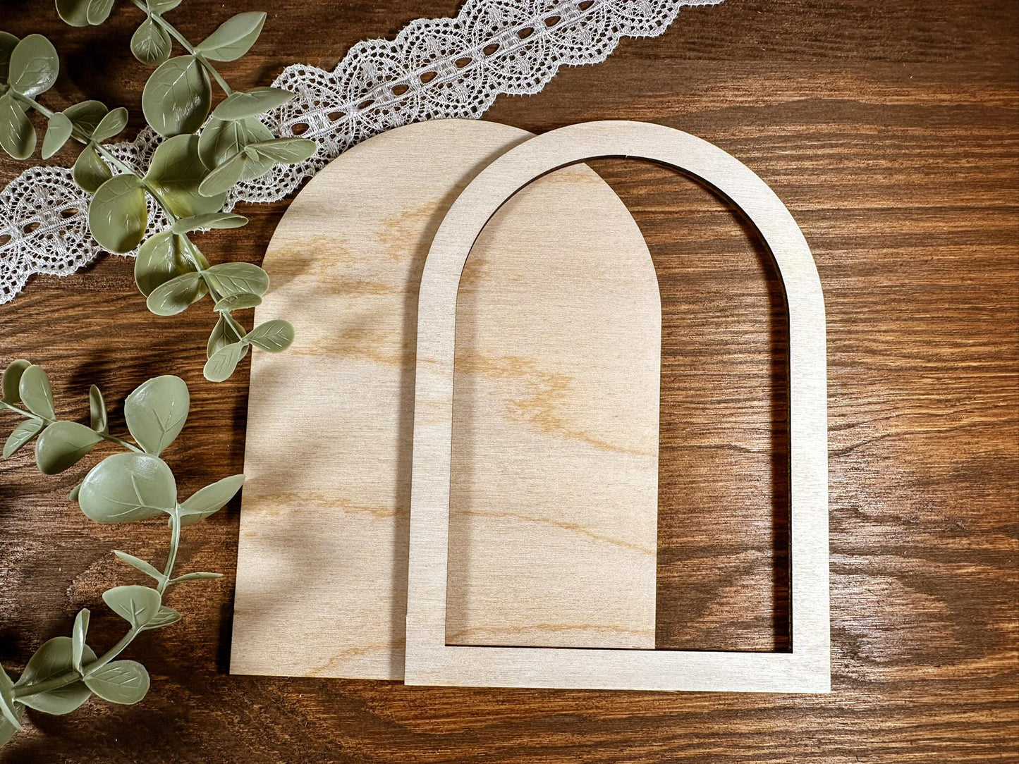 Two wooden arches on a wooden surface with eucalyptus leaves and lace.