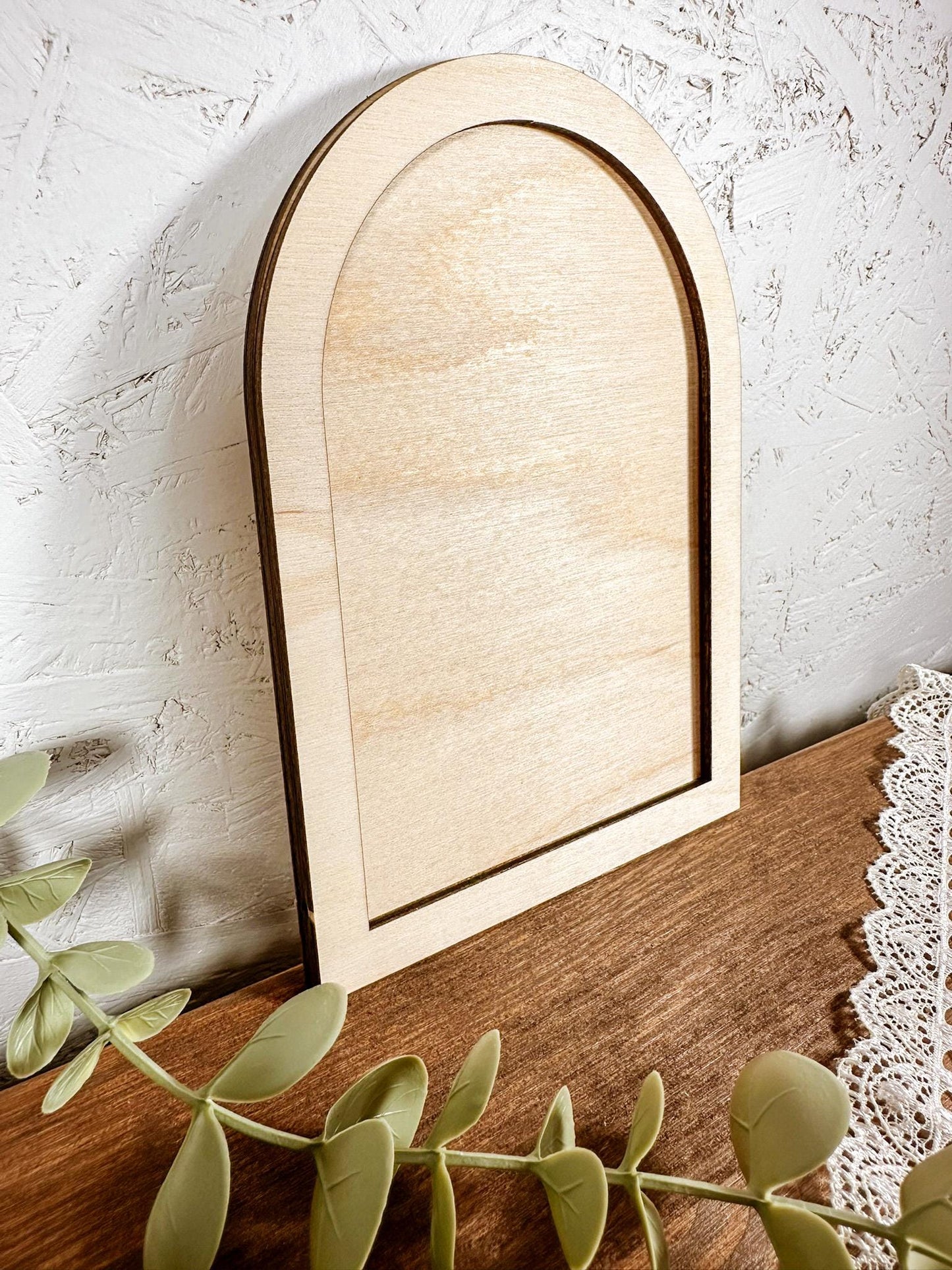 Wooden mirror with an arch top on a wooden surface with a white textured wall background