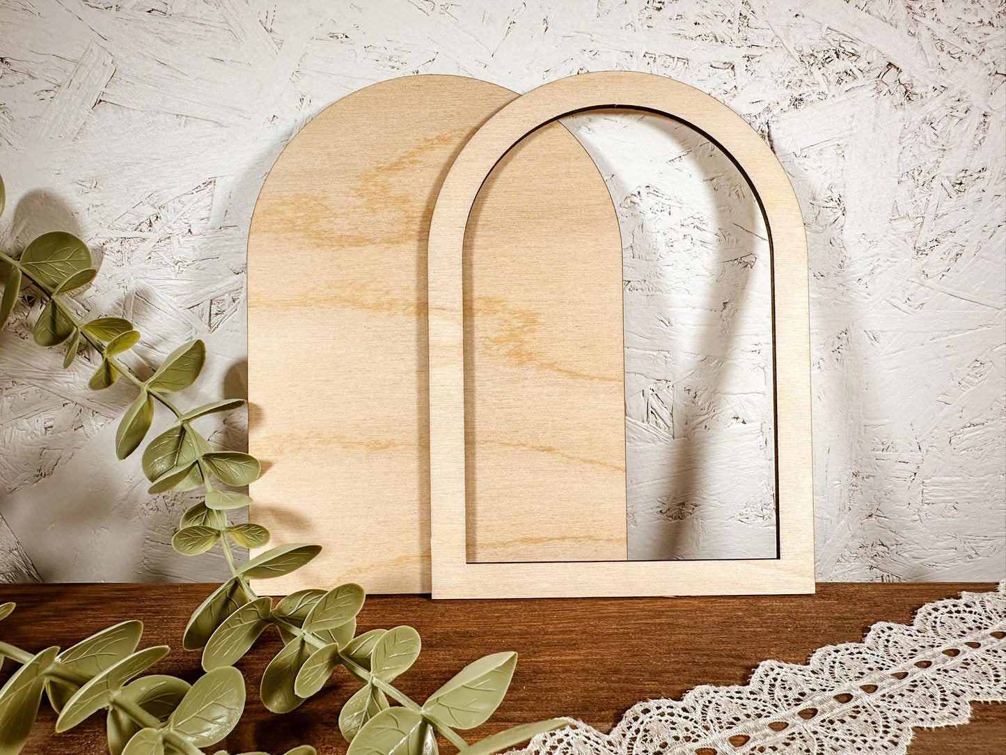 Two wooden arches on a wooden surface with eucalyptus leaves and lace.