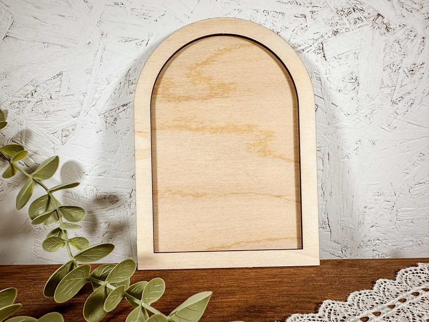 Two wooden arches on a wooden surface with eucalyptus leaves and lace.