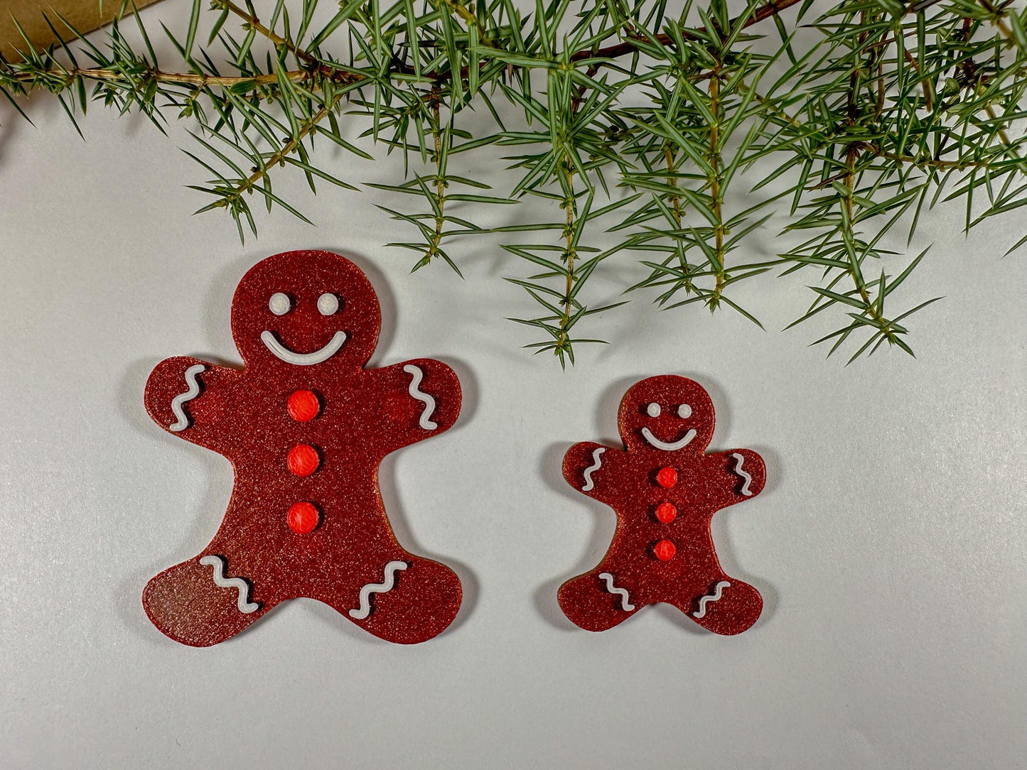 Two red gingerbread man ornaments on a light background with greenery.