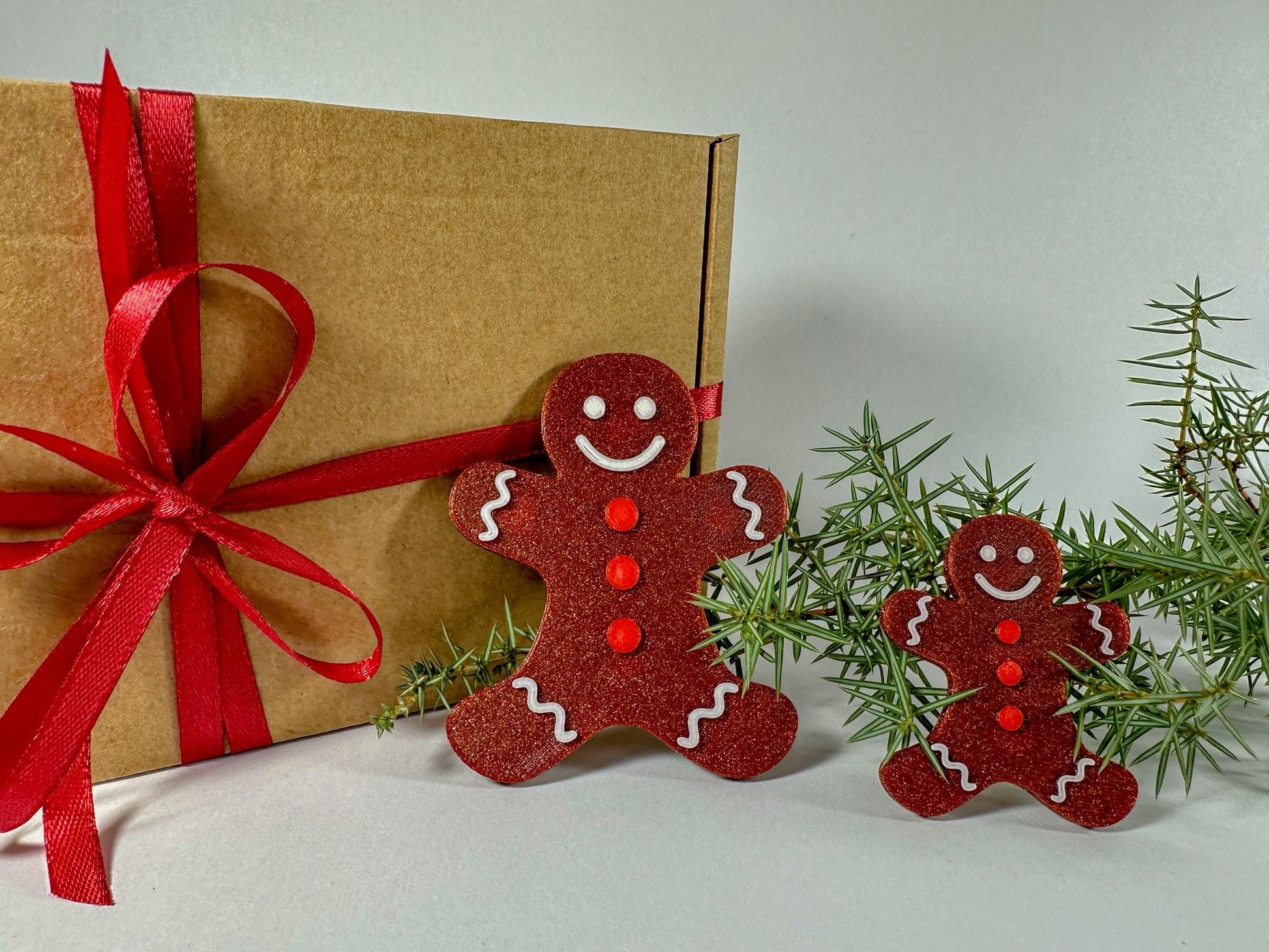 Two red gingerbread man ornaments on a light background with greenery.